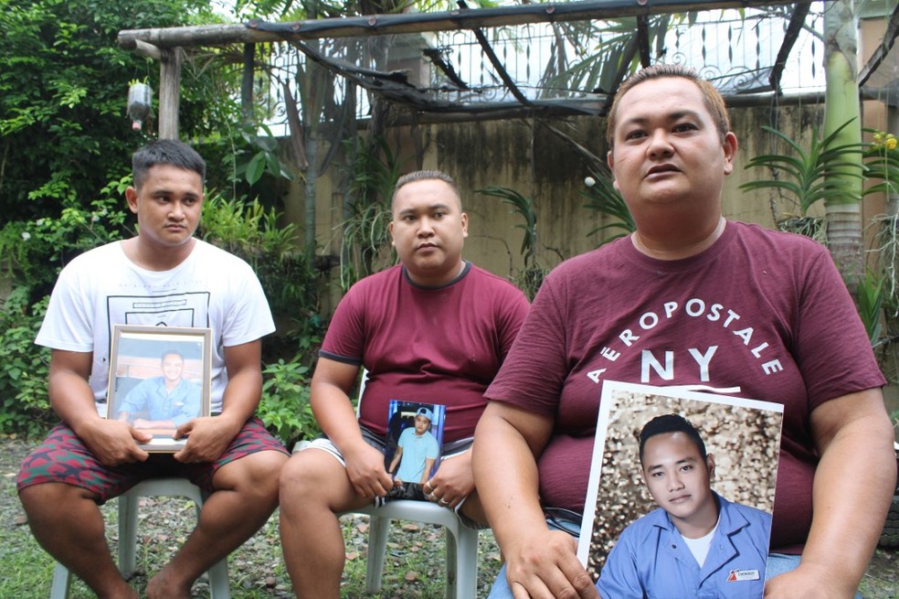 Os irmãos Rocky, Mike e Lorenzo posam para fotos enquanto seguram um retrato de seu irmão Cherokee Capajo em casa em Dingle, província de Iloilo, centro das Filipinas — Foto: AFP